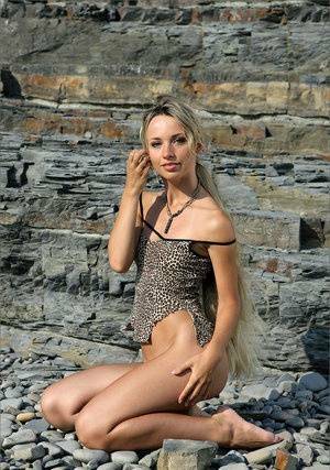 Dirty blonde beauty cradles her tan lined tits while naked against a rock face on dollser.com