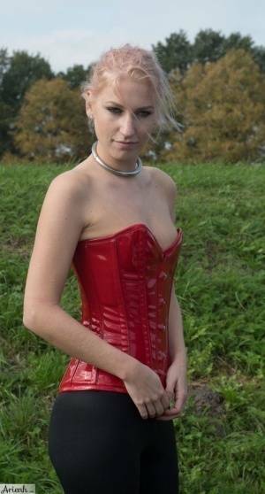 Collared girl Arienh Autumn models a red leather corset while in a field on dollser.com